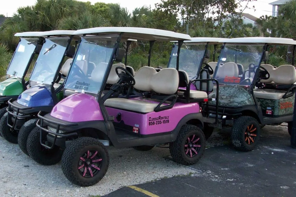 Pink, blue, green and camo golf carts lined up at Classic Rentals in Panama City Beach